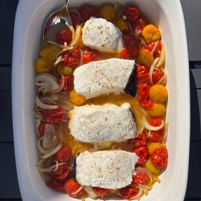 Halibut steaks in a dish with tomatoes and onions, with a serving spoon inside
