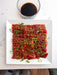 Raw tuna with sesame seeds and green onions on a white plate with a side of soy sauce.