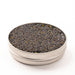 Side view of an opened silver tin containing black and brown pearls on a white surface.