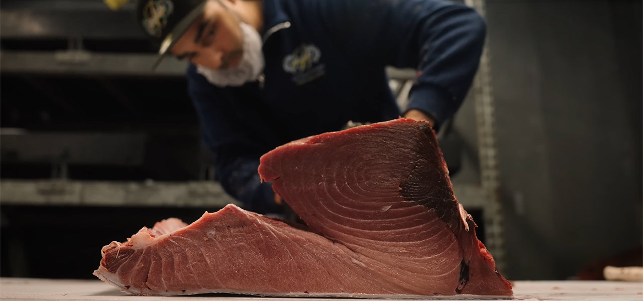 Man inspecting a large cut of fish in a warehouse setting