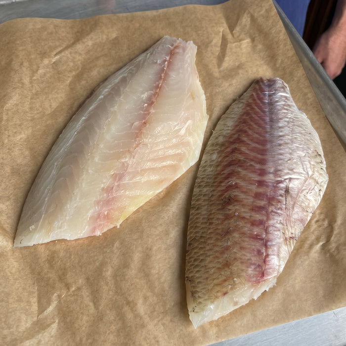 Two raw dry aged Madai fillets on a baking tray with parchment paper.