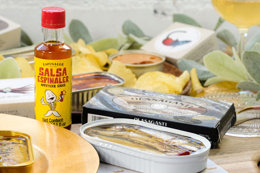 Open tin of Olasagasti Basque Anchovies shown with a bottle of hot sauce as a serving suggestion