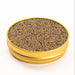 Side view of an opened gold tin containing shiny amber brown pearls on a white surface.