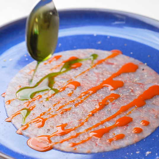Thinly sliced Gambero Rosso prawn carpaccio from Browne Trading Company, arranged on a plate with garnishes.