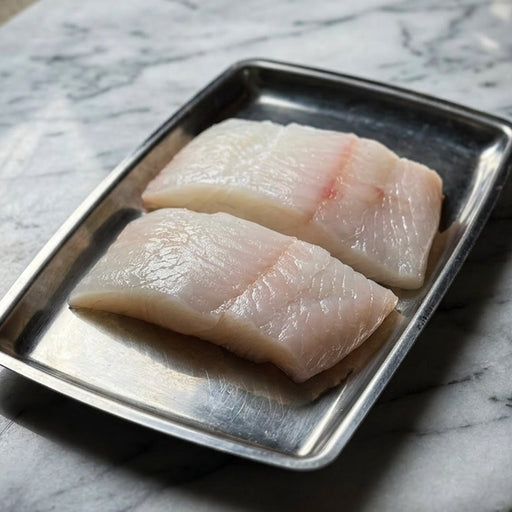 Two pieces of raw halibut on a metal tray on a marble surface