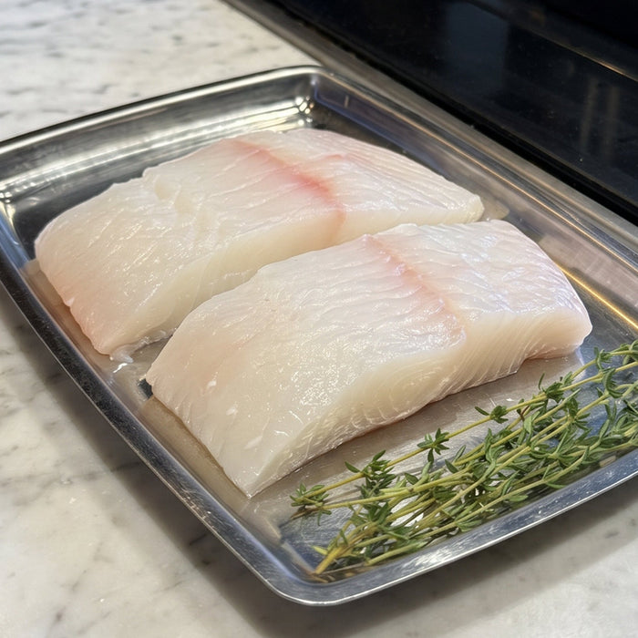 Raw halibut steaks  on a tray with thyme on a kitchen counter.