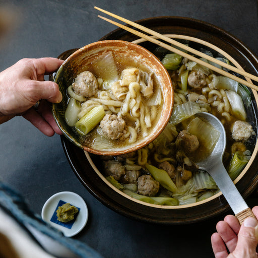 Kagura Green Yuzu Kosho jar next to a bowl of udon noodles in a hot pot, showcasing the spicy citrus paste from Kagura No Sato.