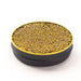 Side view of an opened black tin with a gold band containing brown and gold pearls on a white surface.