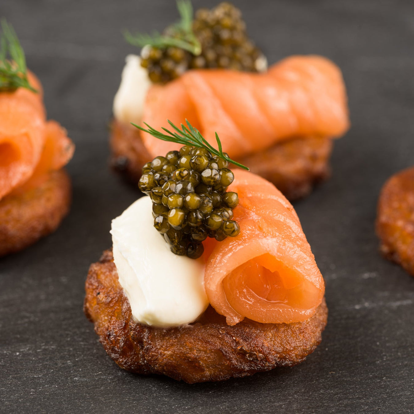 Smoked salmon canapés with caviar on potato latke a dark surface