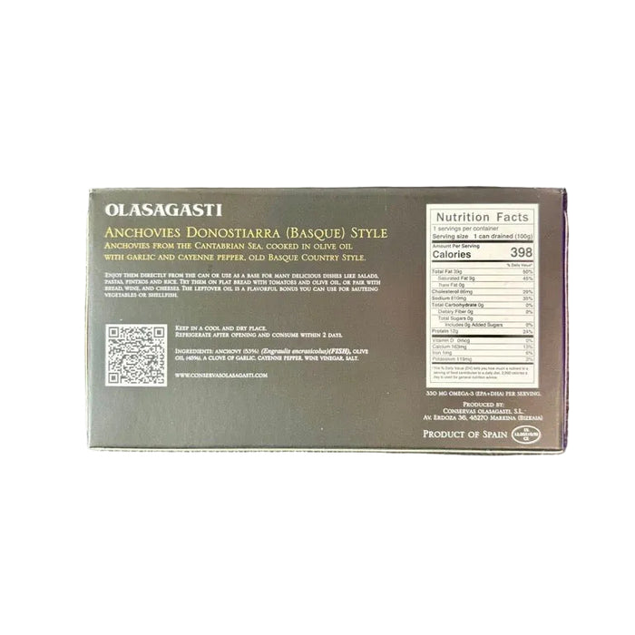 The back of a dark gray Olasagasti Anchoville Dorynchaster (Bassake) style canned food package, resting on a black textured leather surface with a wooden table visible at the bottom.