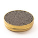 Side view of a gold tin containing small, brown pearls on a white surface.