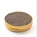 Side view of an opened gold tin containing shiny brown pearls on a white surface.