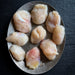 Nine raw skate cheek pieces arranged on a round silver metal plate against a dark textured slate background.