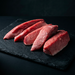 5 pieces of raw meat on a black slate board