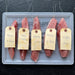 Five raw cuts of bluefin tuna collar "kama toro" set on a clear plastic tray, each with a handwritten paper tag labeled 'kama' and different weights, set against a dark slate background.