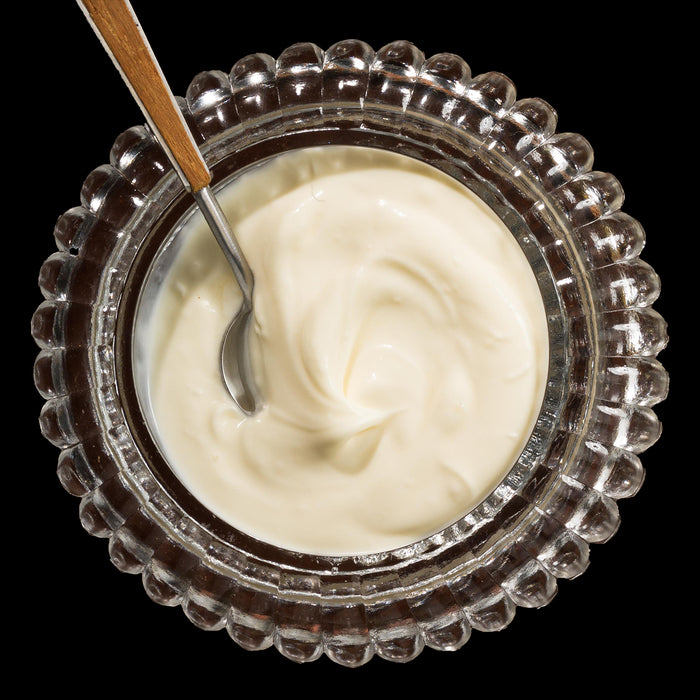 Top-down view of a clear glass bowl with a scalloped edge filled with smooth creme fraiche and a small spoon with a wooden handle resting inside.