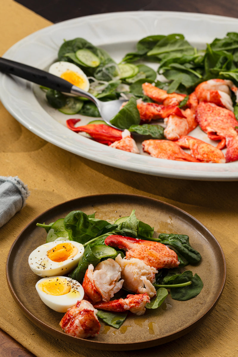 Plated Maine Lobster Meat served with fresh lettuce and halved boiled eggs seasoned with black pepper in a cobb salad