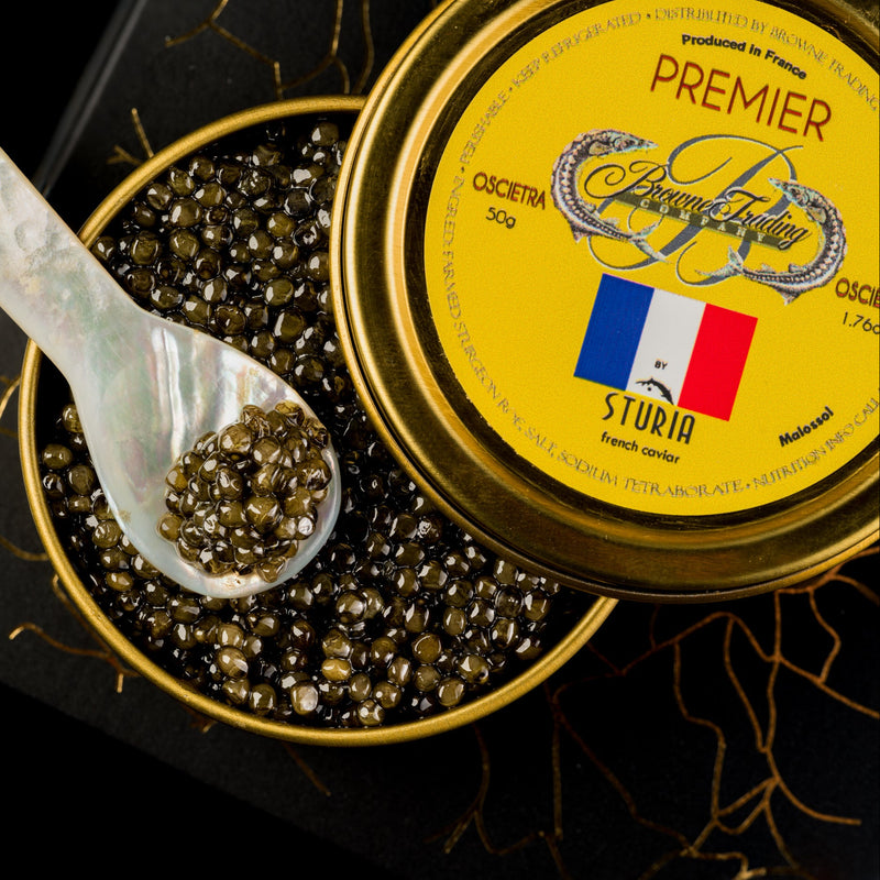 Close-up of a tin of premium French Sturia Premier Osetra caviar with a mother-of-pearl spoon scooping the caviar pearls, displayed as part of the French Gift Box.