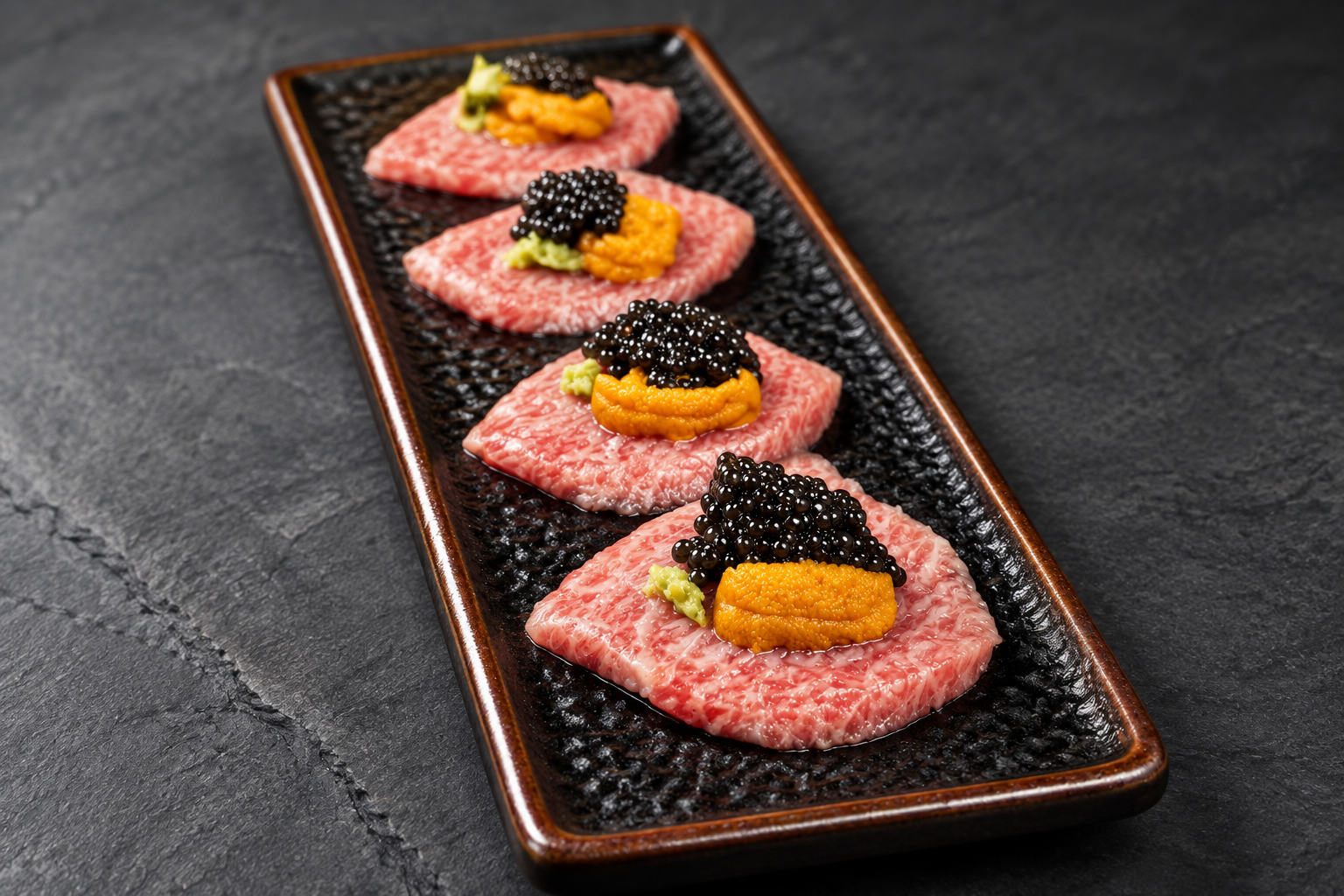 raw meat with orange uni and black caviar on a black textured plate